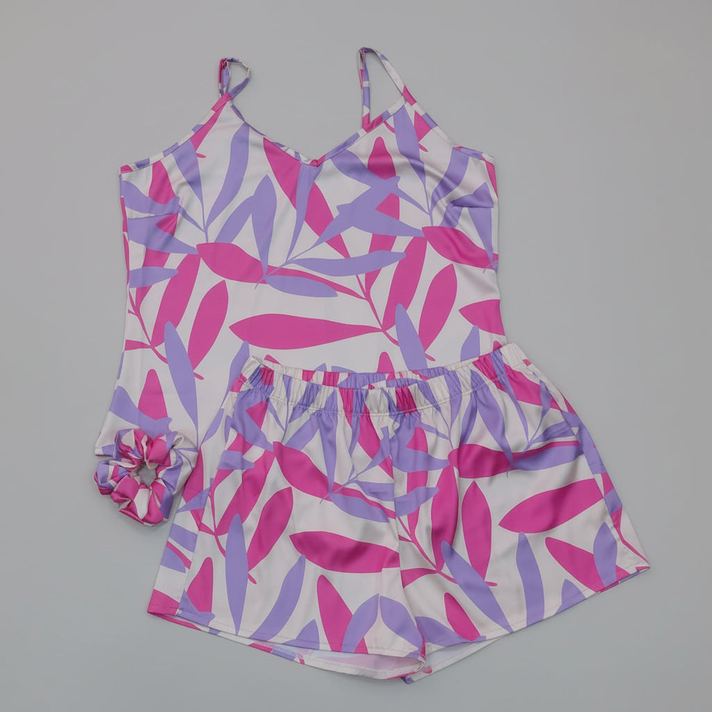 A two-piece matching set consisting of a sleeveless camisole top and shorts, featuring a vibrant pink and purple leaf pattern on a white background, laid flat on a gray wood plank floor.